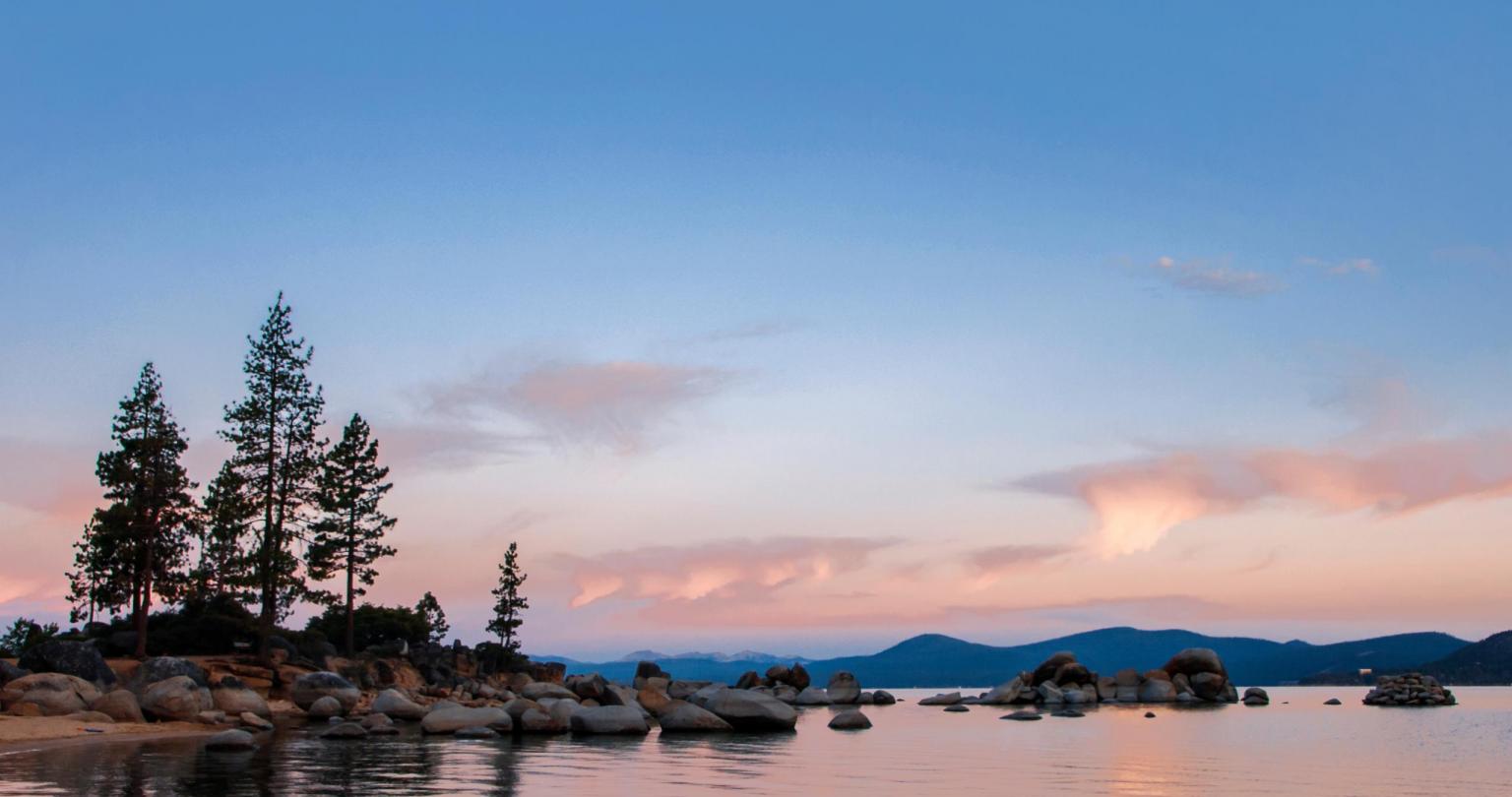 The sun warms the clouds in the sky over Lake Tahoe in summer at sunrise, Lake Tahoe State Park, Sand Harbor, Washoe County Nevada