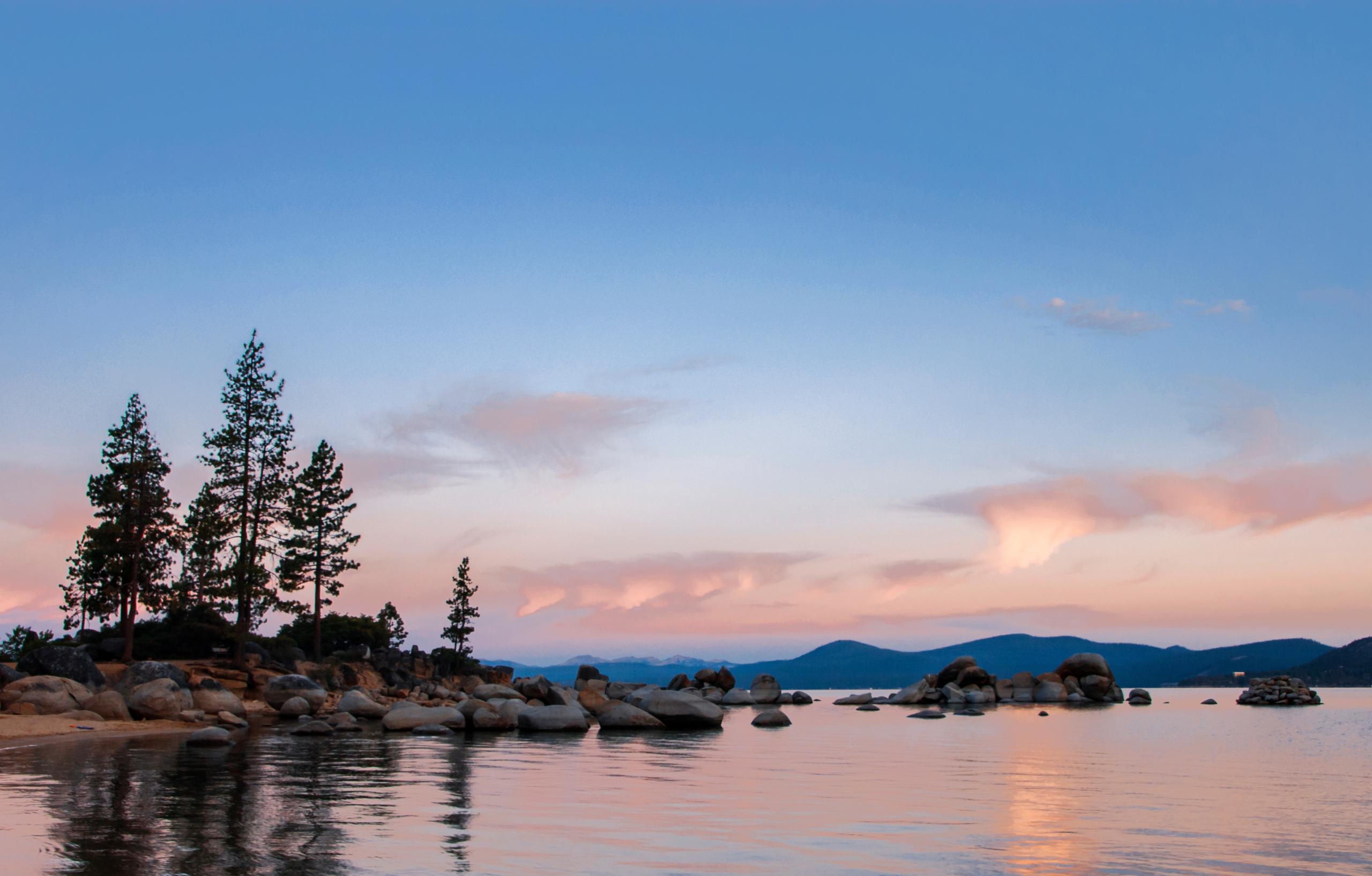 The sun warms the clouds in the sky over Lake Tahoe in summer at sunrise, Lake Tahoe State Park, Sand Harbor, Washoe County Nevada